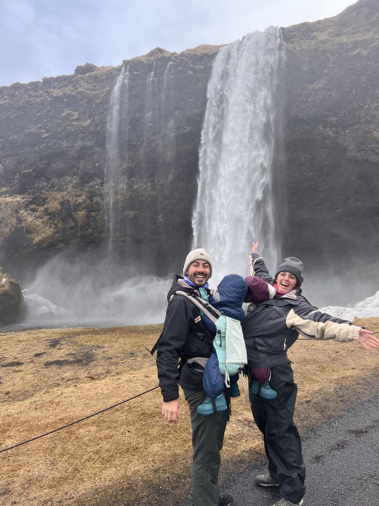 Familia con bebés en porte en catarata en islandia